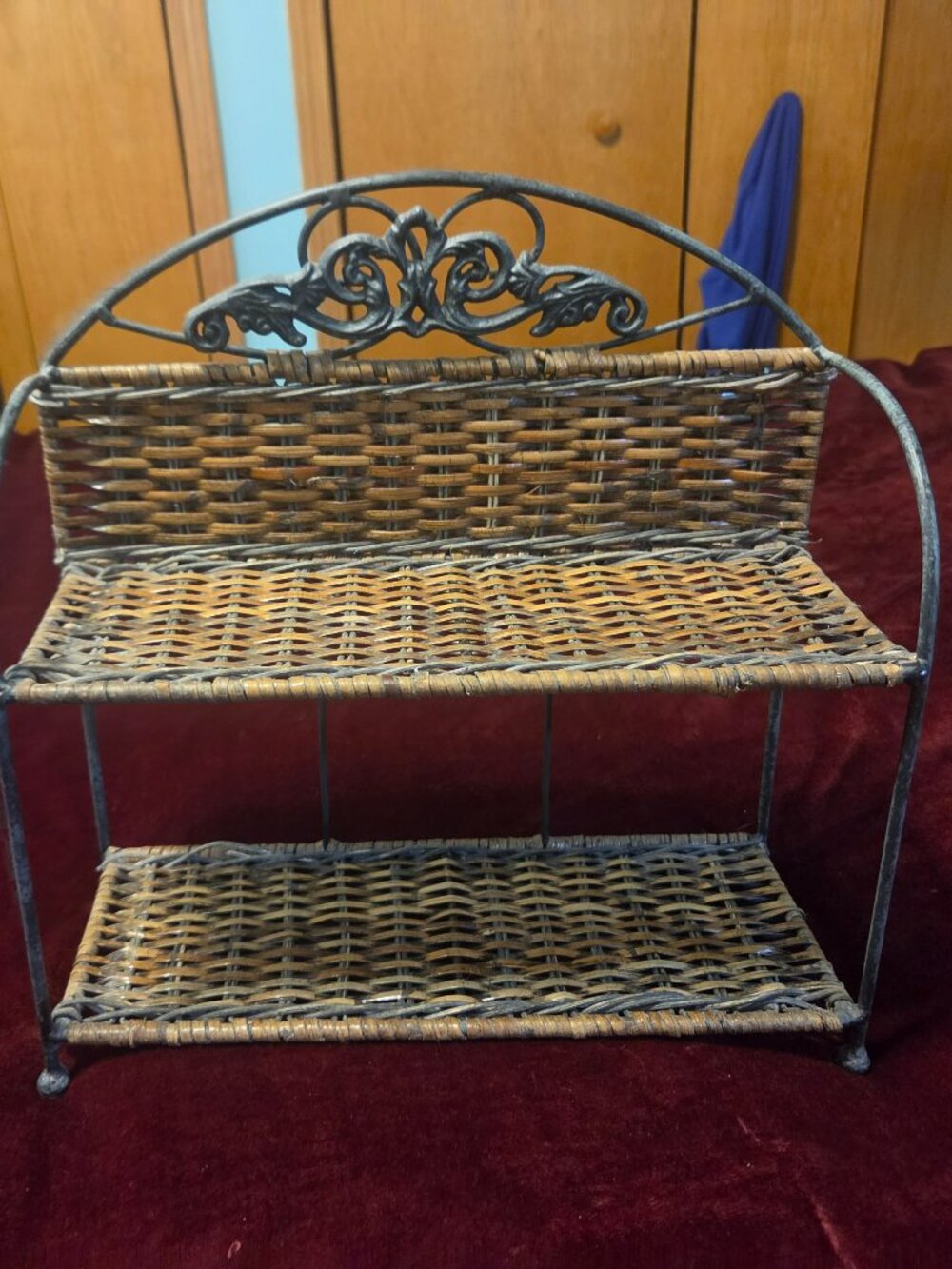 two tier wicker shelf with metal frame adorned with scrollwork some wear
